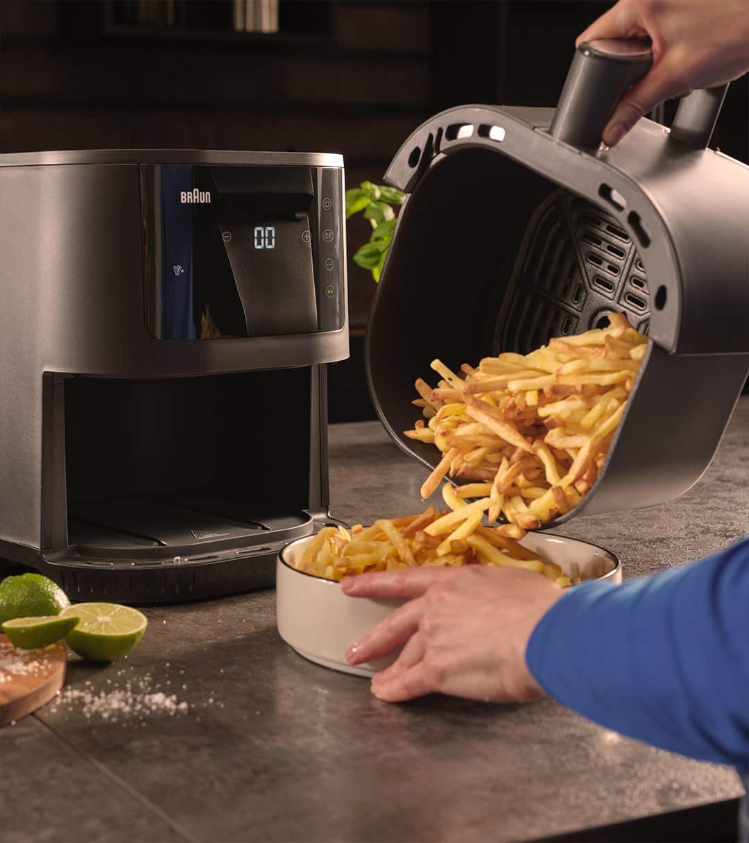 Close-up of Braun's MultiFry 3 Air fryer. On the right, a person is pouring golden, crispy pommes frites from the air fryer’s removable drawer into a serving bowl.