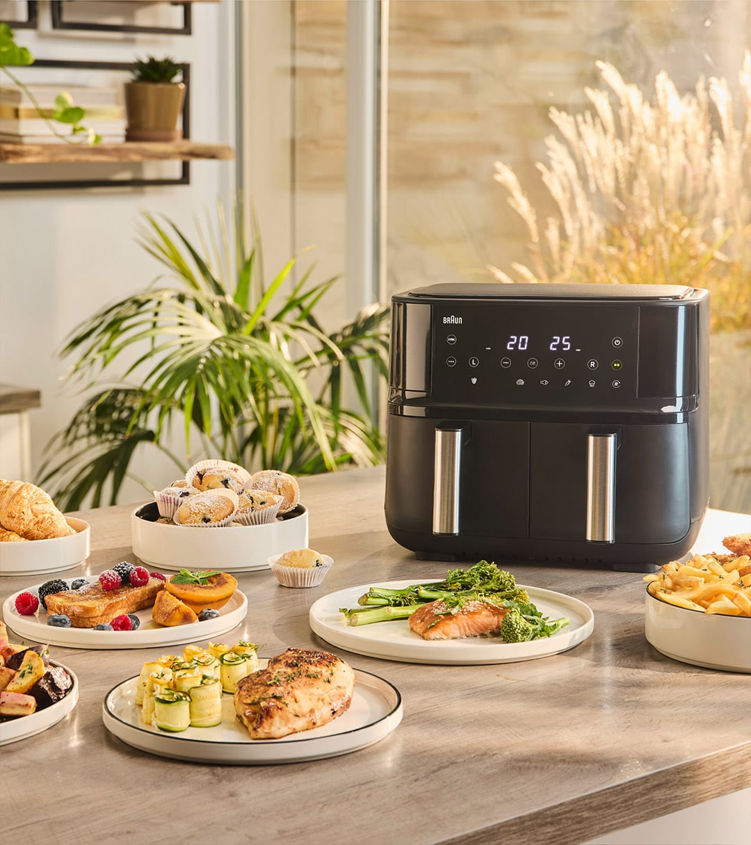 Braun TwinCook 3 Air fryer on a table, surrounded by plates of delicious food.