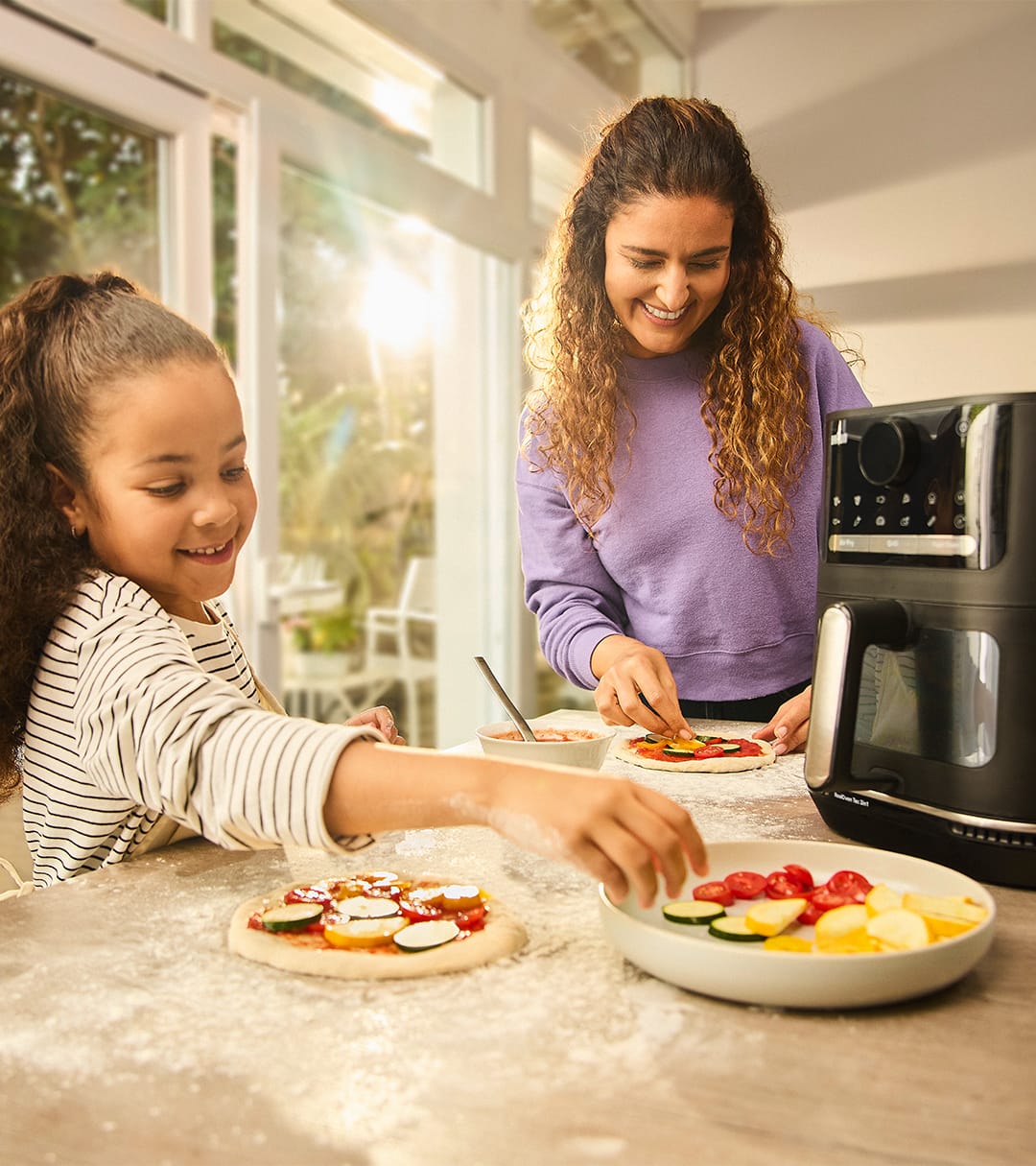 Young girl helps her mother prepare a pizza with the Braun TwinCook 3 Air fryer.