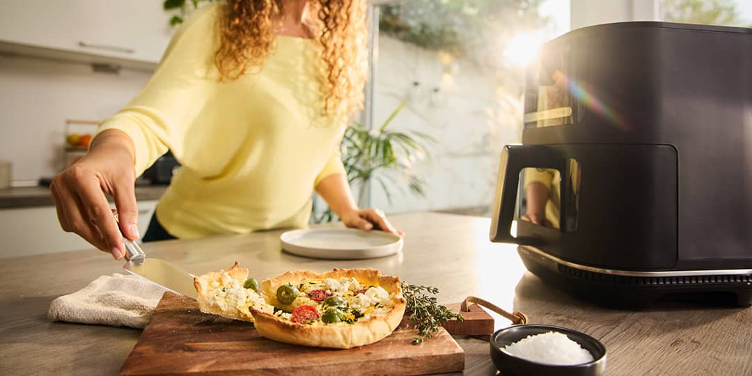 A woman is taking a piece of crispy quiche out of the drawer of a Braun MultiFry Air fryer.