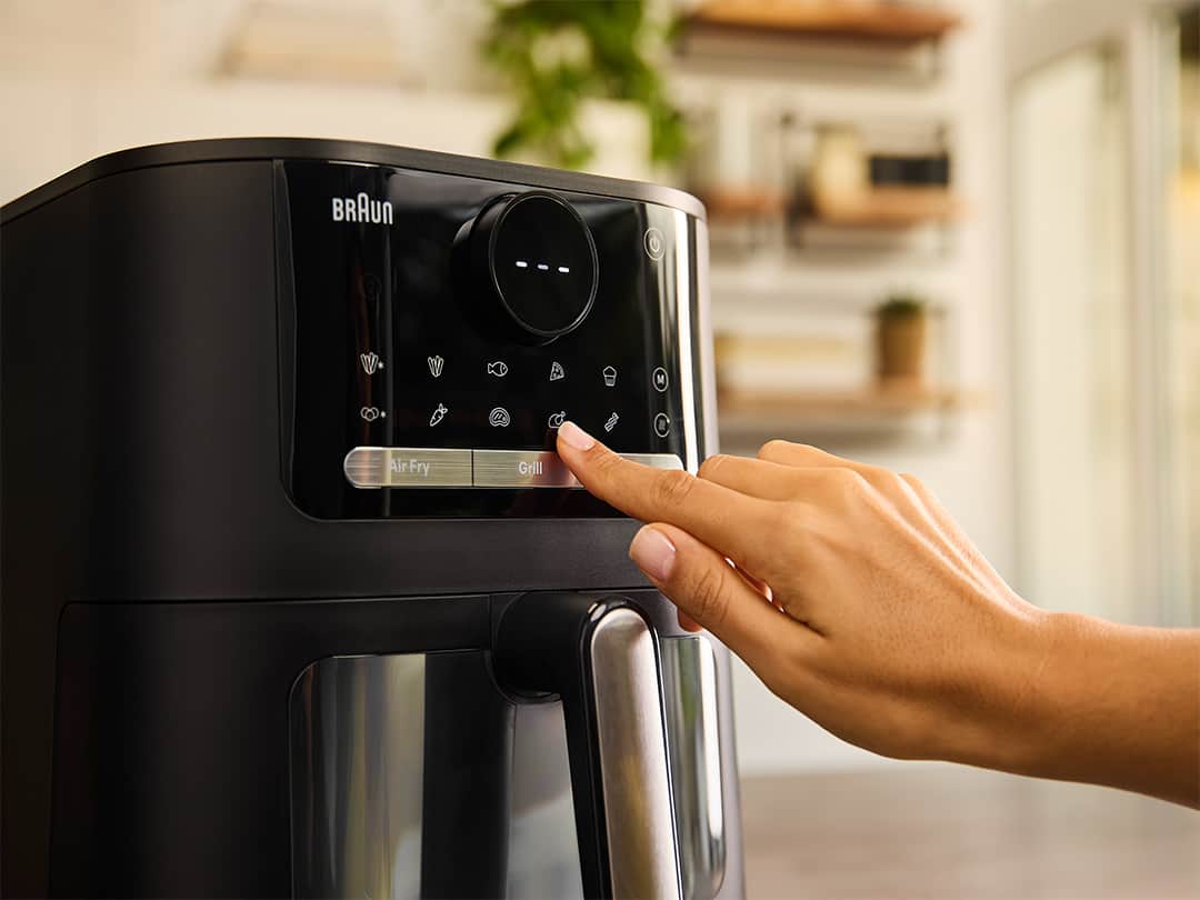 Close-up of the Braun MultiFry 5 with its digital display. A woman hand presses one of the numerous automatic cooking programmes.