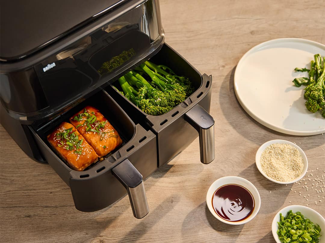 The 2 drawers of the Braun TwinCook 3 hot air fryer are pulled out. The left drawer is filled with perfectly cooked salmon, the right drawer with crispy, steamed broccoli.
